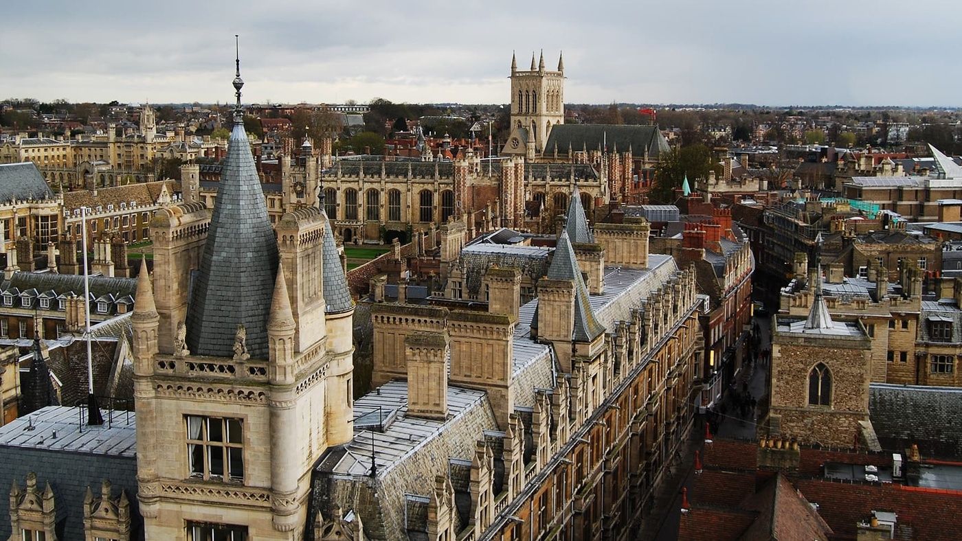 A stone tower overlooks a city. Numerous buildings with steep roofs and spires are densely packed together. The context is a historic European city.